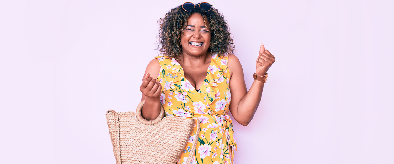 The welcome to empowered expression image features and upbeat model of African American descent grinning of joy and clenching her fists in excitement. She is wearing a yellow midi dress that features blossoms all over it as a design.